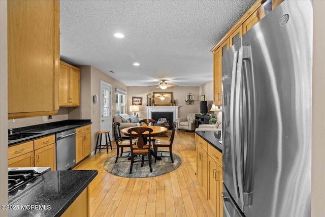 kitchen with a textured ceiling, stainless steel appliances, a fireplace, open floor plan, and light wood-type flooring