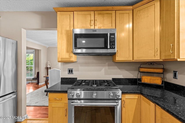 kitchen with crown molding, stainless steel appliances, a textured ceiling, dark stone countertops, and wood finished floors