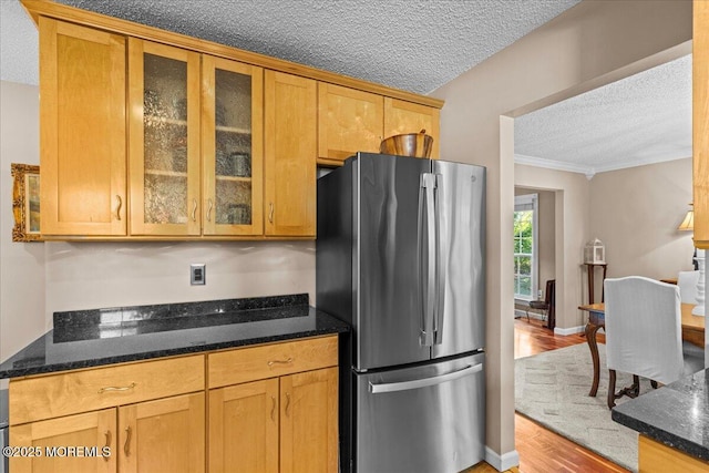 kitchen featuring glass insert cabinets, freestanding refrigerator, light wood-style floors, a textured ceiling, and dark stone counters