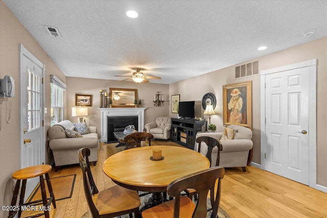 dining space with light wood-style floors, visible vents, and a glass covered fireplace