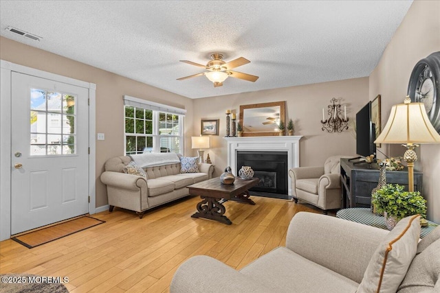 living room with light wood-style floors, a fireplace with flush hearth, visible vents, and a textured ceiling