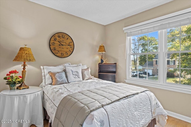 bedroom with a textured ceiling, baseboards, and wood finished floors