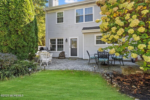 rear view of house with a chimney, a lawn, and a patio