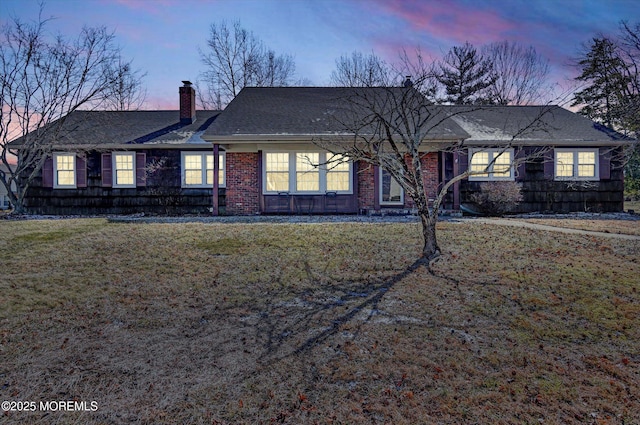 ranch-style home with a yard, brick siding, and a chimney