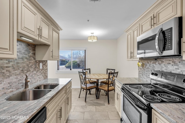 kitchen with appliances with stainless steel finishes, a sink, light stone counters, and cream cabinets