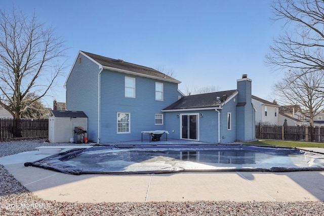 rear view of property featuring a storage shed, fence, a fenced in pool, and an outbuilding