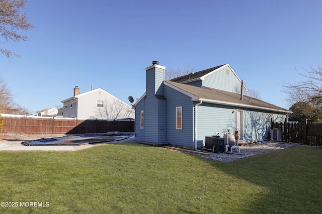 back of property with a fenced backyard, a chimney, and a lawn