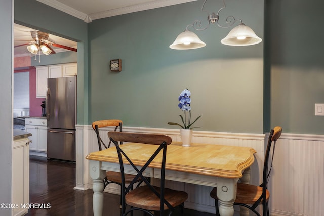 dining room with ornamental molding, wainscoting, dark wood finished floors, and a ceiling fan