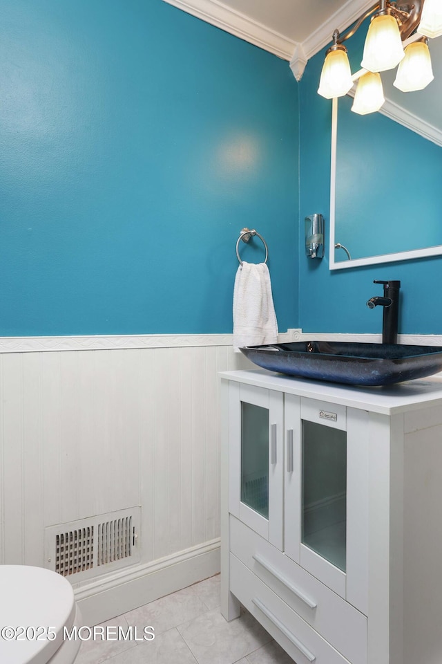 bathroom featuring a wainscoted wall, crown molding, visible vents, toilet, and a sink