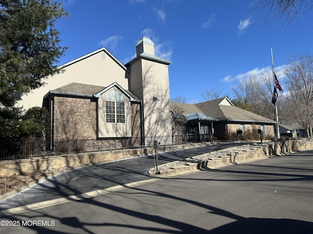 view of front facade with a shingled roof, brick siding, and fence