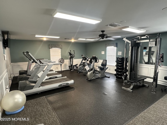 gym with ceiling fan, wainscoting, visible vents, and a decorative wall