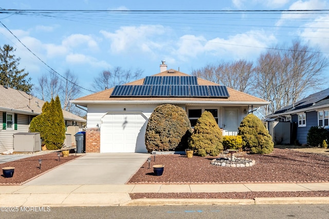 view of front of house with a garage, brick siding, concrete driveway, roof mounted solar panels, and a chimney