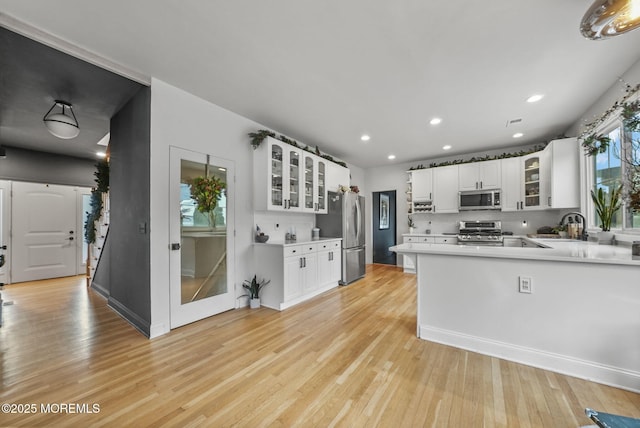 kitchen featuring light wood-style flooring, glass insert cabinets, appliances with stainless steel finishes, light countertops, and white cabinetry