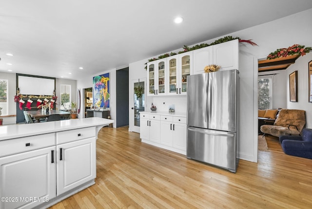 kitchen with white cabinets, light countertops, freestanding refrigerator, light wood finished floors, and glass insert cabinets