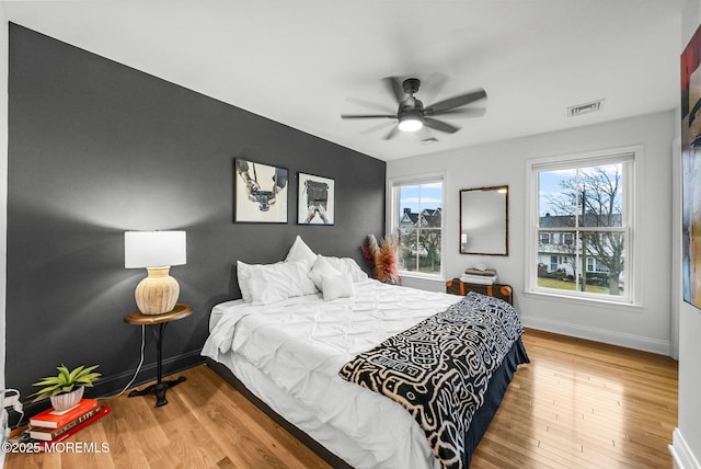 bedroom with a ceiling fan, visible vents, baseboards, and wood finished floors