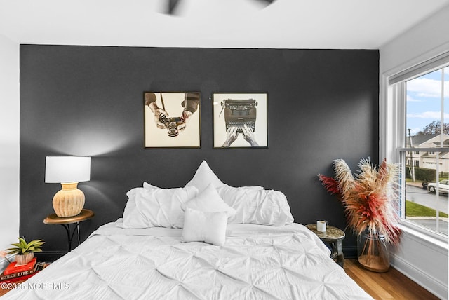 bedroom with an accent wall, wood finished floors, and baseboards