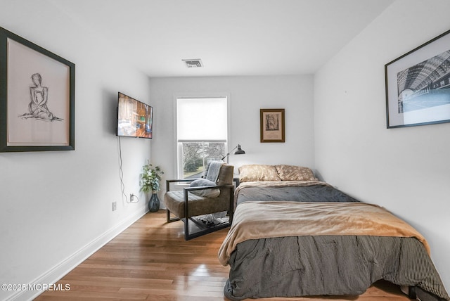 bedroom with baseboards, visible vents, and wood finished floors