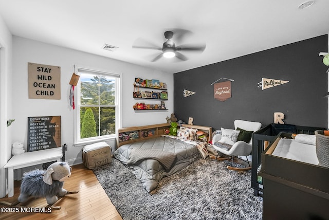 bedroom with a ceiling fan, visible vents, and wood finished floors