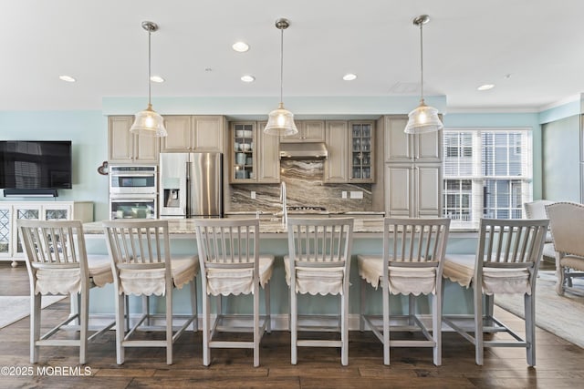 kitchen featuring glass insert cabinets, a kitchen breakfast bar, stainless steel appliances, under cabinet range hood, and pendant lighting