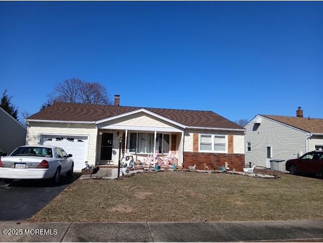 view of front of house featuring brick siding, aphalt driveway, an attached garage, a porch, and a front yard