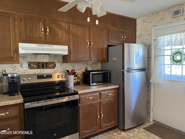 kitchen with under cabinet range hood, stainless steel appliances, visible vents, light countertops, and wallpapered walls