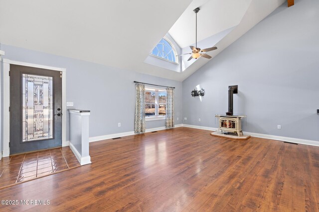 foyer featuring ceiling fan, high vaulted ceiling, baseboards, dark wood-style floors, and a wood stove