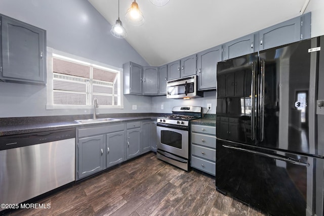 kitchen with lofted ceiling, stainless steel appliances, a sink, dark countertops, and decorative light fixtures