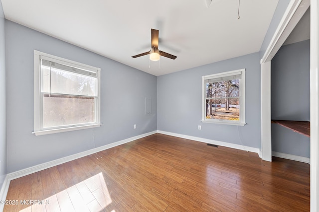 empty room with ceiling fan, visible vents, baseboards, and wood finished floors