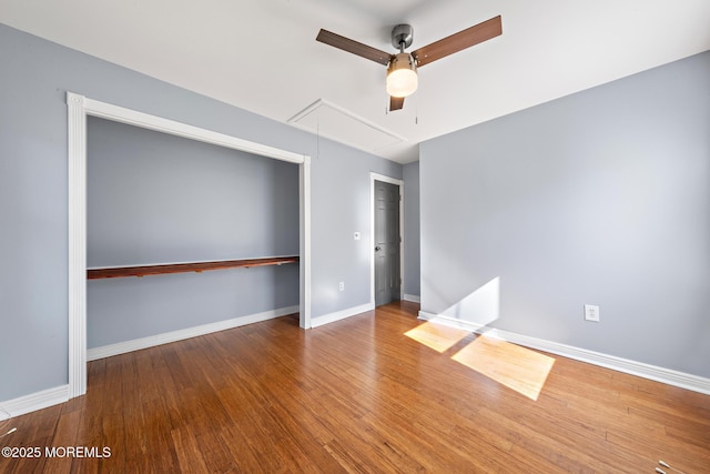 empty room featuring ceiling fan, wood finished floors, attic access, and baseboards