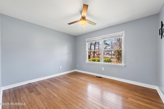 empty room featuring visible vents, wood finished floors, a ceiling fan, and baseboards