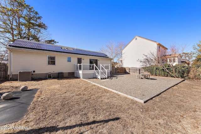 rear view of house featuring a patio, central air condition unit, roof mounted solar panels, metal roof, and a fenced backyard