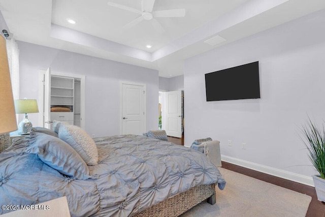 bedroom featuring recessed lighting, wood finished floors, a ceiling fan, baseboards, and a tray ceiling