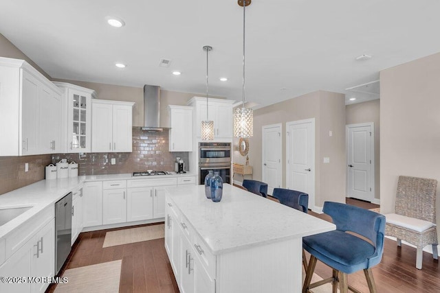 kitchen featuring a kitchen breakfast bar, dark wood-type flooring, a center island, stainless steel appliances, and wall chimney range hood