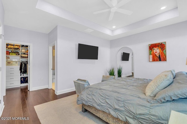 bedroom with baseboards, a raised ceiling, hardwood / wood-style flooring, a walk in closet, and a closet