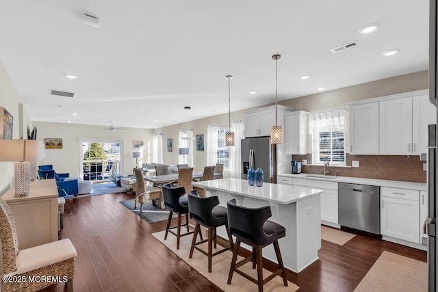 kitchen featuring visible vents, appliances with stainless steel finishes, open floor plan, a kitchen breakfast bar, and a center island