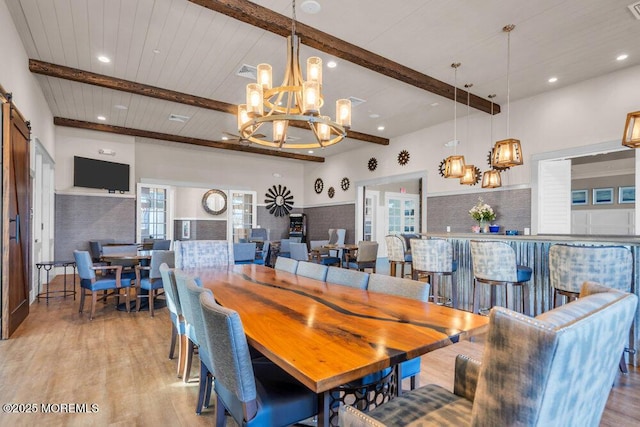 dining area with a barn door, light wood-style flooring, and beam ceiling