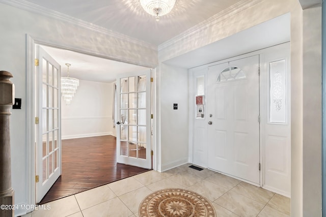 entryway with french doors, a notable chandelier, light tile patterned floors, ornamental molding, and baseboards