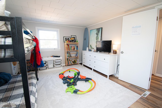 bedroom with ornamental molding, visible vents, baseboards, and wood finished floors