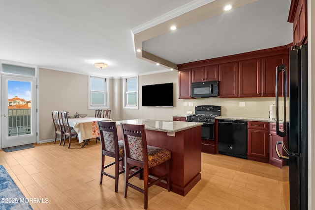 kitchen featuring reddish brown cabinets, a center island, light stone counters, and black appliances