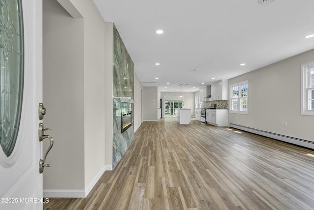 unfurnished living room featuring light wood-style flooring, recessed lighting, a baseboard heating unit, a premium fireplace, and baseboards