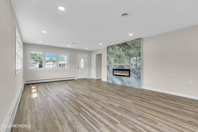 unfurnished living room with a baseboard heating unit, a premium fireplace, recessed lighting, and light wood-style floors