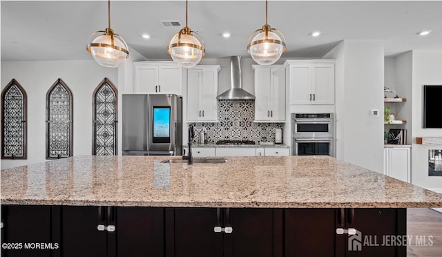 kitchen featuring visible vents, wall chimney exhaust hood, decorative light fixtures, light stone countertops, and stainless steel appliances