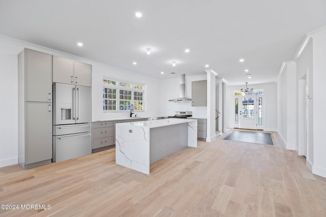 kitchen with high end fridge, a center island, gray cabinetry, wall chimney range hood, and a sink
