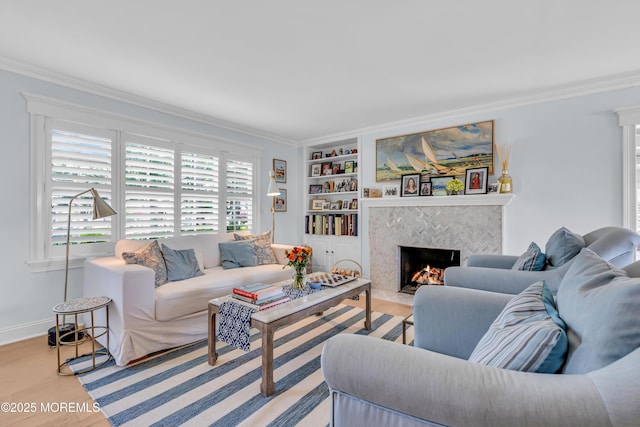 living room with built in features, a fireplace, light wood-style flooring, ornamental molding, and baseboards