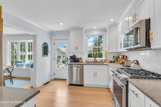 kitchen with crown molding, backsplash, appliances with stainless steel finishes, white cabinetry, and a sink