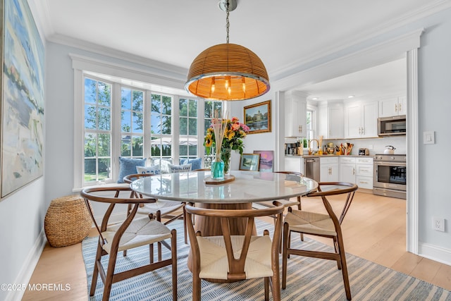 dining area with light wood-style floors, a wealth of natural light, crown molding, and baseboards