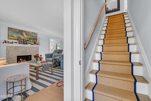 stairway with ornamental molding, wood finished floors, and a tile fireplace