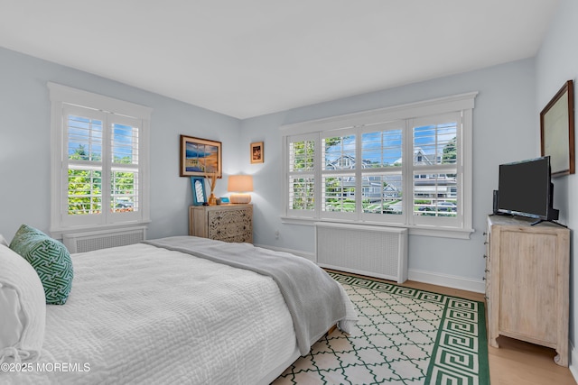 bedroom with baseboards, light wood-style flooring, and radiator heating unit