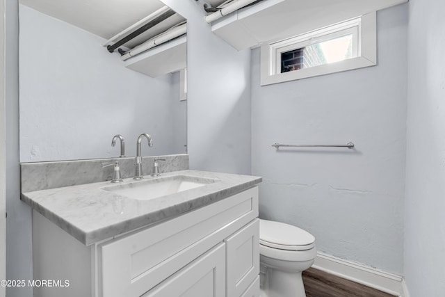 bathroom with toilet, baseboards, wood finished floors, and vanity