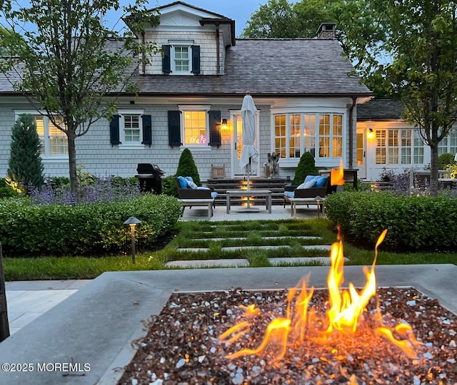 back of house with roof with shingles, a chimney, a fire pit, and a patio